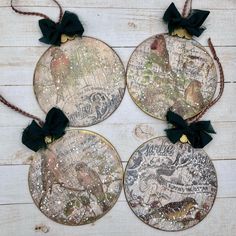 four round ornaments with black bows are on a white wooden surface, one is decorated with an old map