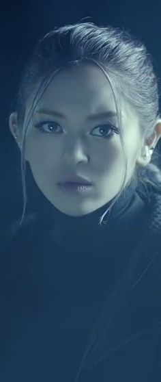 a woman with long hair and blue eyes looks into the camera while standing in front of a dark background