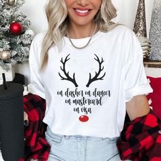 Get into the holiday spirit with a hilarious twist on a classic Christmas saying! This funny Christmas t-shirt features the phrase "On Dasher, On Dancer, On Mastercard, On Visa" with a cute graphic of festive reindeer horns and a red nose. Perfect for those who love to shop 'til they drop during the holiday season, this tee brings humor and style together. WHY YOU'LL LOVE THIS SHIRT: Festive & Funny: The clever play on Santa's reindeer names combined with credit cards adds a fun, modern touch to your holiday wardrobe. Cute Holiday Graphic: Reindeer antlers and a red nose give this shirt an extra dose of festive cheer. Perfect for Shoppers: A must-have for anyone who enjoys holiday shopping, gift-giving, or simply loves a good laugh. Soft & Comfortable: Made from premium quality material th Reindeer Horns, Reindeer Names, Santa's Reindeer, Funny Christmas Tshirts, Reindeer Antlers, Funny Christmas Shirts, Red Nose, Holiday Wardrobe, Santa And Reindeer