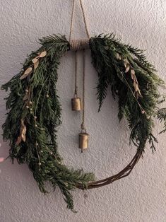 a wreath hanging on the wall with two bells attached to it and evergreen leaves around it