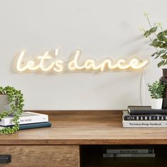 a wooden table topped with books and a plant next to a sign that says let's dance