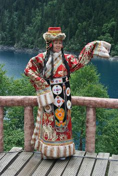 a woman dressed in traditional chinese clothing stands on a balcony overlooking a lake and forest