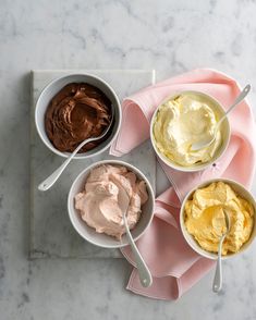 three bowls of ice cream and two spoons on a pink napkin next to each other