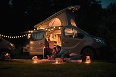 two people sitting in front of a camper at night with lights strung from the roof