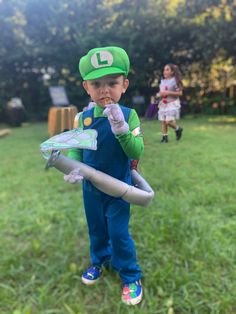 a young boy dressed up as luigi and holding a plastic bat in his hand while standing on the grass