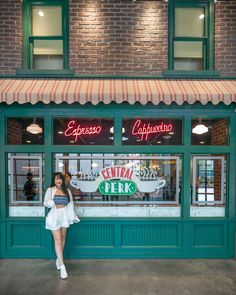 a woman standing in front of a restaurant with green shutters and neon signs on the windows