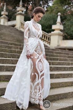 a woman standing on some steps wearing a white dress with long sleeves and high slits