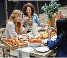 three women sitting at a table with food and drinks