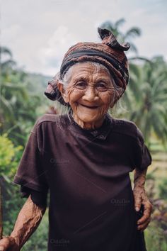 an old woman with wrinkles on her face standing in front of some palm trees