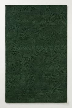 a green rug with flowers and leaves in the center on a white wall behind it