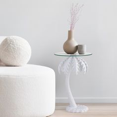 a white table with a vase on it next to a round chair and footstool