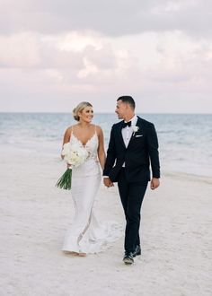 a bride and groom walking on the beach