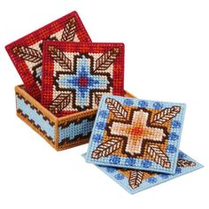 two square coasters with cross designs on them, one in blue and the other in red