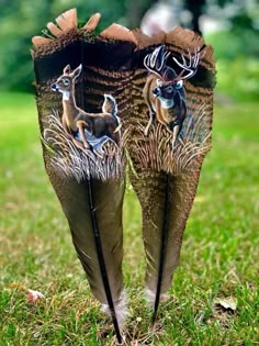 two feathers with pictures of deer and birds on them are standing in the green grass