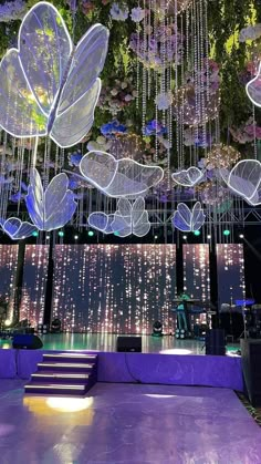 an indoor dance floor with purple lighting and flowers hanging from it's ceiling above