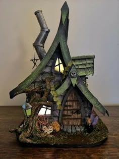 a small house made out of wood and moss with a chimney on the roof is lit up at night