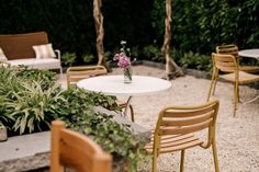 a table and chairs with flowers in a vase sitting on top of it next to some plants