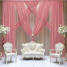 a white couch sitting next to two chairs in front of a pink drapeed wall