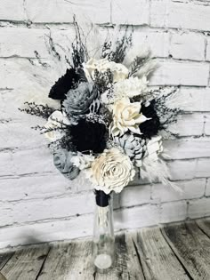 a vase filled with black and white flowers on top of a wooden table next to a brick wall