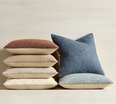 pillows stacked on top of each other in front of a beige wall with a blue pillow