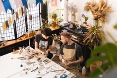 two men sitting at a table working on crafts