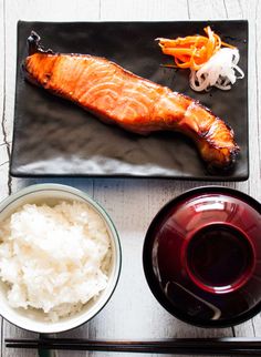 a plate with rice, fish and carrots on it next to chopsticks