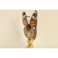 a glass vase with a butterfly on it's head sitting on a gold base