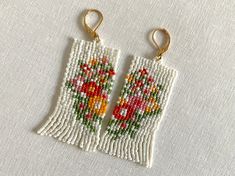 pair of beaded earrings with flowers on white fabric, hanging from gold - plated hooks