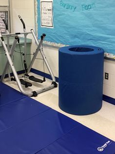 a gym with exercise equipment and blue mats on the floor in front of a bulletin board