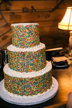 a three tiered cake with sprinkles on the side and a lamp next to it