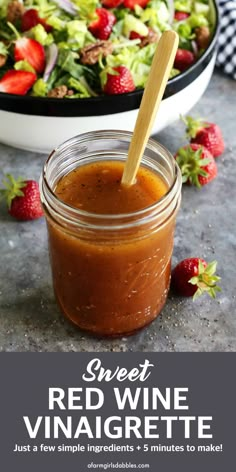 a jar filled with red wine vinaigrette next to a bowl of strawberries