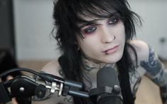 a man with black hair and piercings on his face sitting in front of a microphone