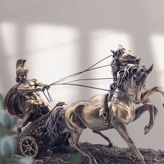 a statue of a man riding on the back of a horse pulling a cart with two horses