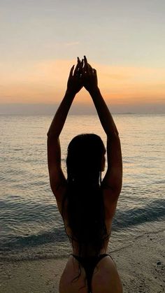 a woman standing on top of a sandy beach next to the ocean at sun set