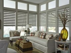 a living room filled with white furniture and windows covered in blind shades on top of them