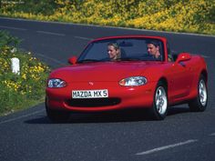 two people in a red sports car driving down the road