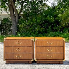 two wooden dressers sitting next to each other on top of a cement ground with trees in the background