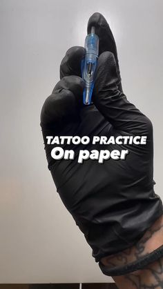 tattoo practice on paper written on the back of a hand wearing black gloves and holding an electronic device in it's palm