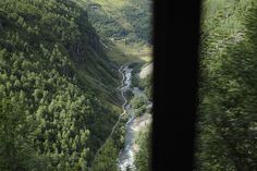 the view from inside a train looking down on a river running through a valley surrounded by trees