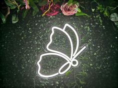 a neon butterfly sitting on top of green grass next to pink roses and greenery