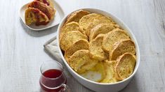 a white dish filled with food next to a glass of wine and another bowl full of bread