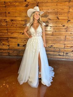 a woman standing in front of a wooden wall wearing a white dress and cowboy hat