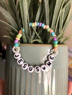 a person holding a potted plant with some beads on it and the words jesus me spelled