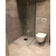 a bathroom with a toilet, shower and tiled walls in grey tones on the floor