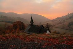 an old church sits in the middle of a field with mountains in the background at sunset