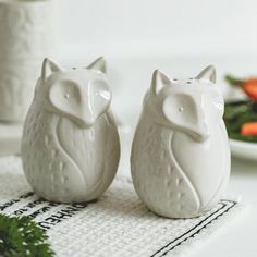 two white ceramic owl figurines sitting on top of a table next to carrots