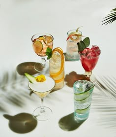 several different types of drinks are arranged on a white surface with shadows from palm leaves