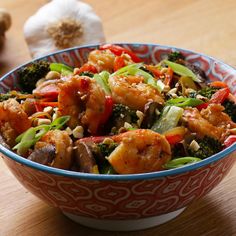 a bowl filled with shrimp and vegetables on top of a wooden table next to garlic