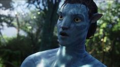 a man with blue paint on his face and chest in front of trees, looking at the camera