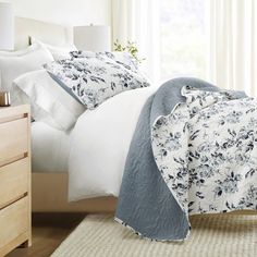 a bed with white and blue comforters in a bedroom next to a window,